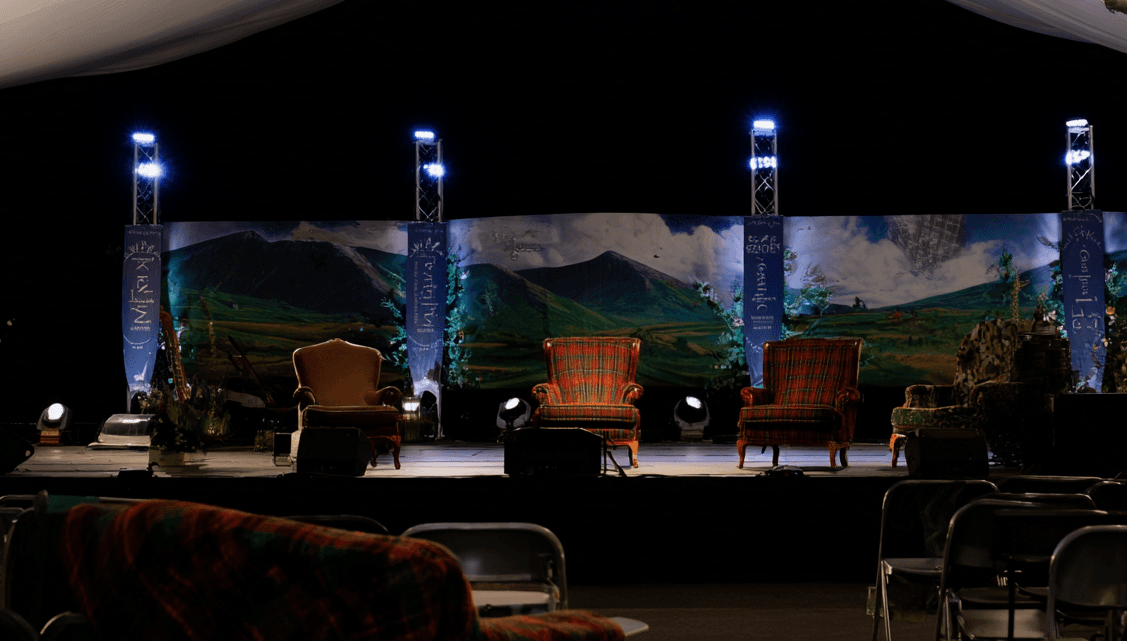 Empty festival stage with purple lighting and Highland backdrop